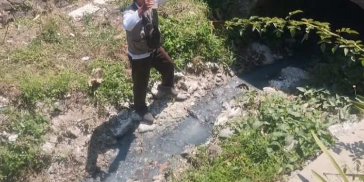 Seorang pegiat lingkungan mengambil dan menguji sampel cairan limbah yang mengalir di saluran air pinggir jalan ruas Mentoro–Tulakan, Kabupaten Pacitan, Jumat (23/10/2026). (Foto: Istimewa)